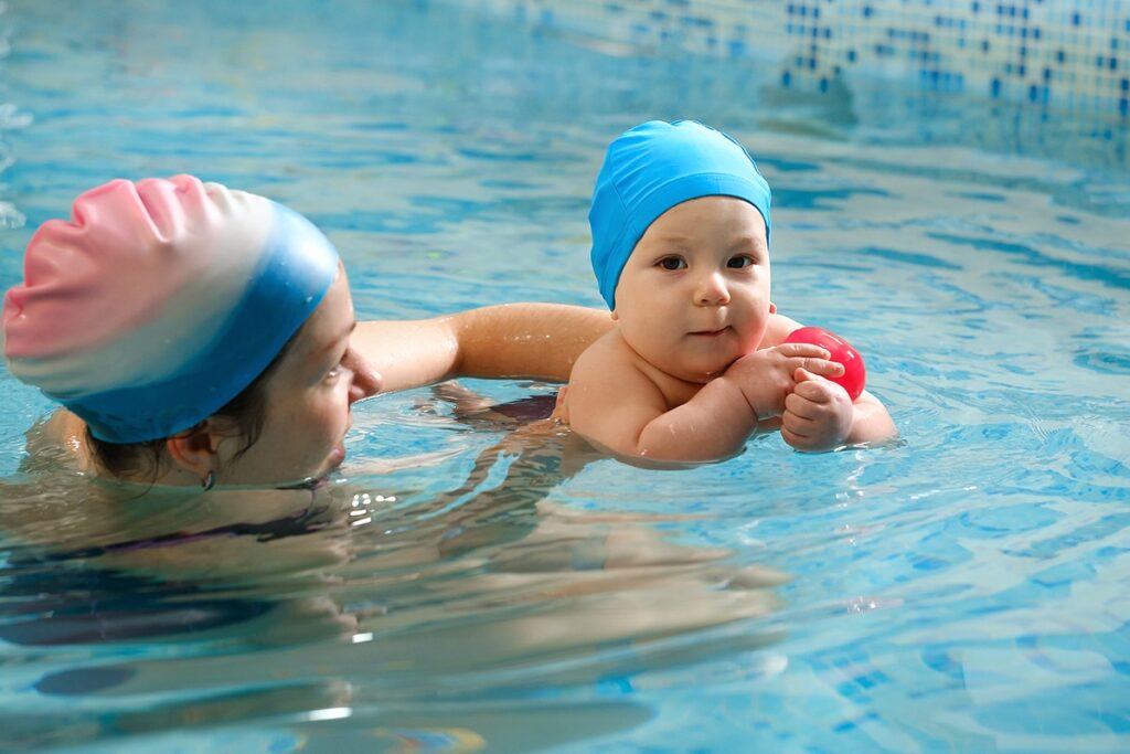 a baby in the pool being taught how to swim by her swimming coach 